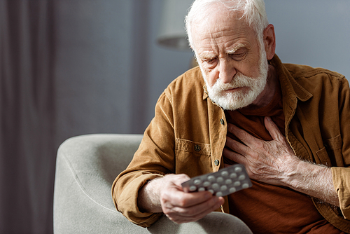 senior man feeling bad, touching chest and holding pills