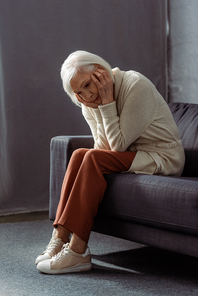 depressed, lonely senior woman holding hands on face while sitting on sofa