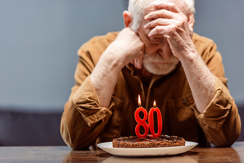 depressed, lonely senior sitting near birthday cake with number eighty