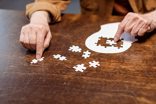 partial view of senior man playing jigsaw puzzle as dementia therapy