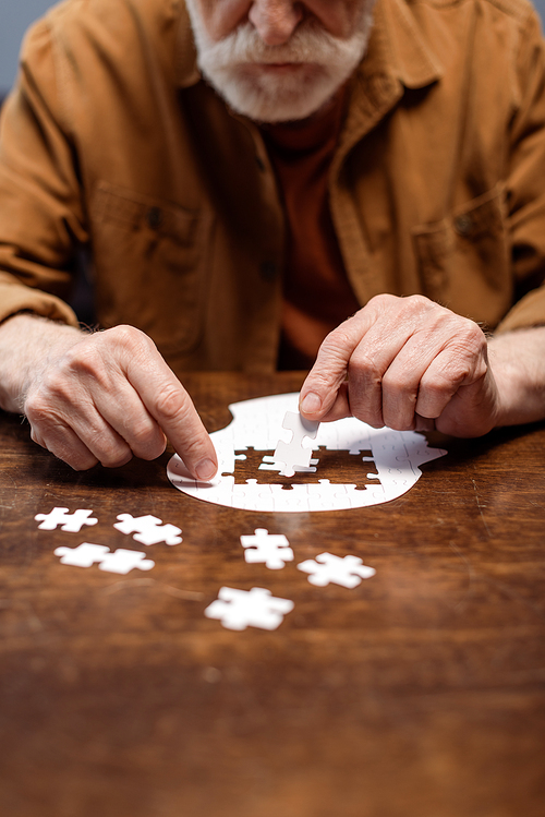 cropped view of senior man playing jigsaw puzzle for dementia rehabilitation