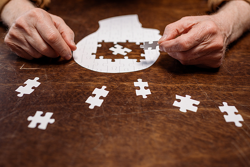 cropped view of ill senior man collecting jigsaw puzzle for dementia therapy