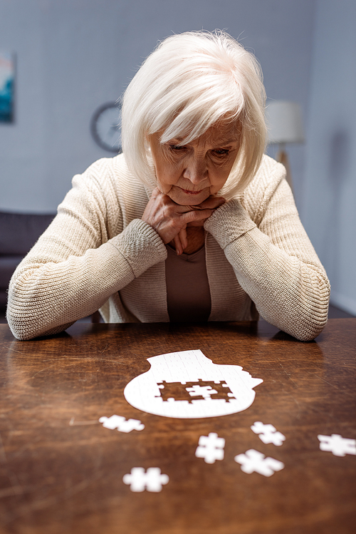 sick senior woman thinking while collecting jigsaw puzzle as dementia therapy
