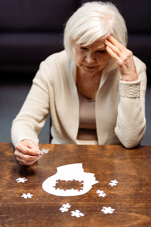 senior woman touching head while playing puzzle as dementia rehabilitation