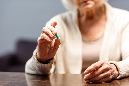 partial view of senior woman holding pill, selective focus