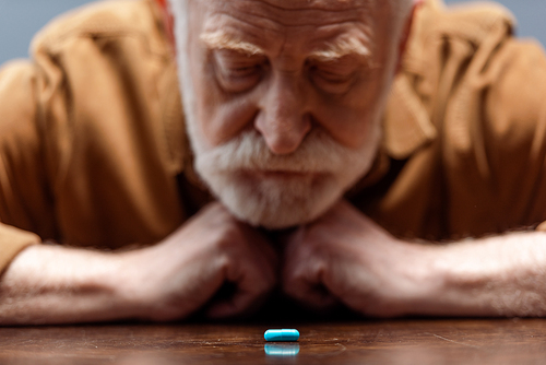 selective focus of old man looking at pill on table