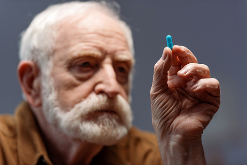 selective focus of sad senior man holding pill