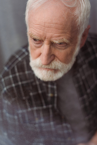 selective focus of depressed senior man looking away through window glass