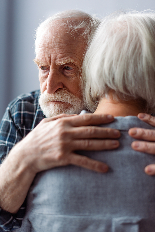 senior man, suffering from dementia, hugging wife and looking away