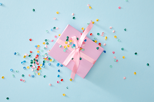 top view of colorful confetti near pink gift box on blue background