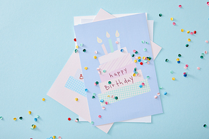top view of colorful confetti near birthday greeting cards on blue background