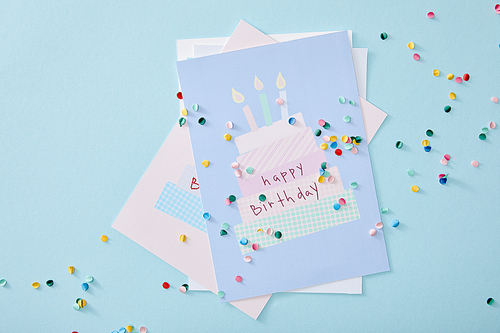 top view of colorful confetti near birthday greeting cards on blue background