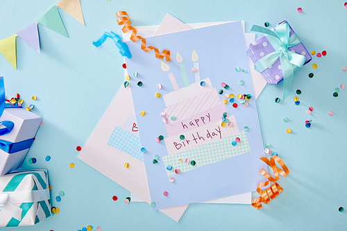 top view of colorful confetti near gift boxes and birthday greeting cards on blue background