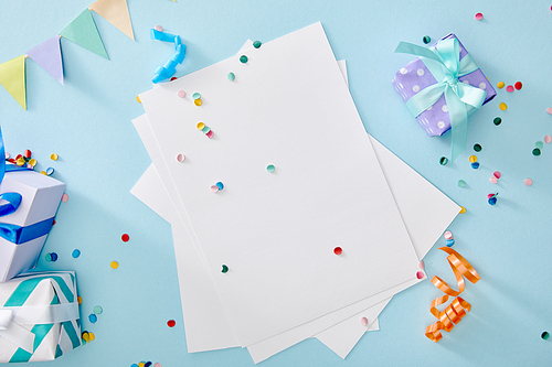 top view of colorful confetti near blank paper and gift boxes on blue background