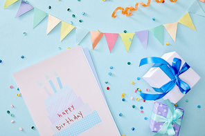 top view of colorful confetti near gift boxes and birthday greeting card on blue background