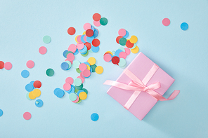 top view of colorful confetti near pink present on blue background
