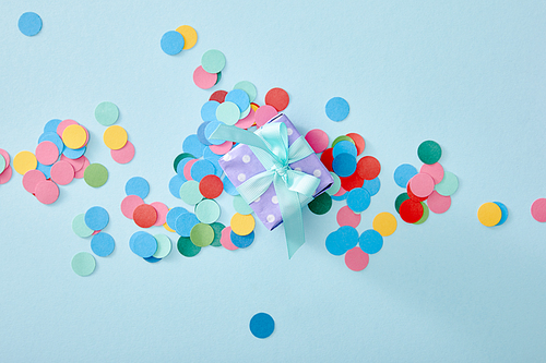 top view of colorful confetti near present on blue background
