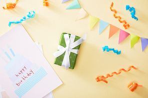top view of festive colorful confetti and gift with happy birthday greeting card on beige background