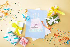 top view of festive colorful confetti, gifts and happy birthday greeting card on beige background