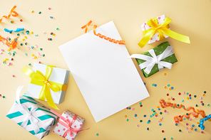 top view of festive colorful confetti and presents near blank paper on beige background