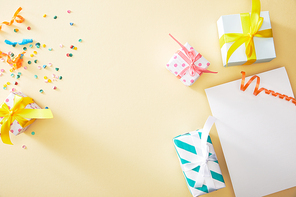 top view of festive colorful confetti and presents near blank paper on beige background