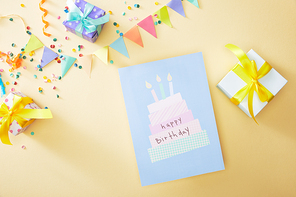 top view of festive colorful confetti and gift boxes near happy birthday greeting card on beige background
