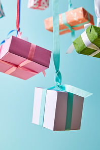 selective focus of festive colorful gift boxes hanging on ribbons isolated on blue