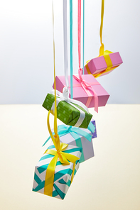 festive colorful gift boxes hanging on ribbons on grey and yellow background