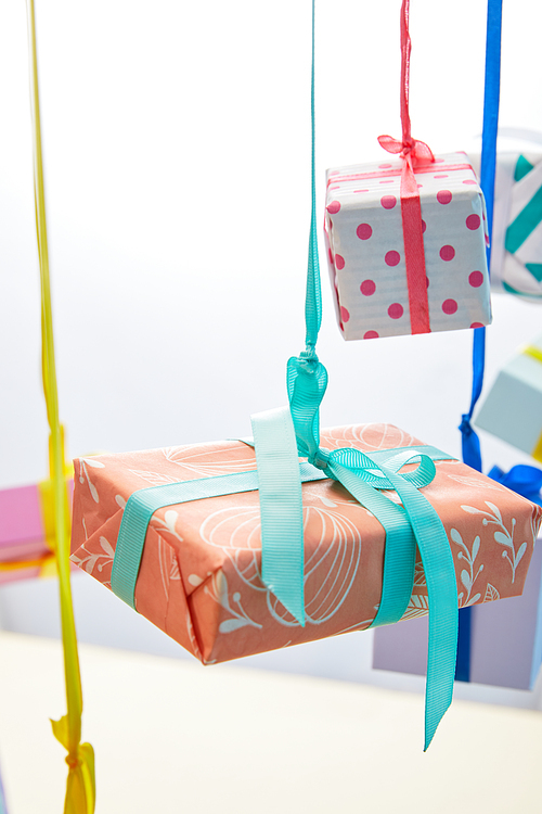 selective focus of festive colorful gift boxes hanging on ribbons on grey and yellow background