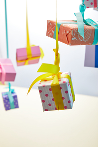 selective focus of festive colorful gift boxes hanging on ribbons on grey and yellow background