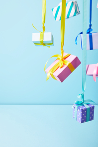 festive colorful gift boxes hanging on ribbons on blue background
