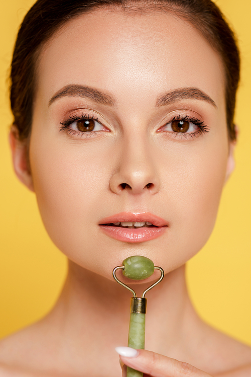 portrait of beautiful woman using jade roller on face isolated on yellow