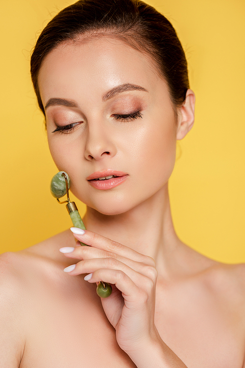 beautiful naked woman using jade roller on face isolated on yellow