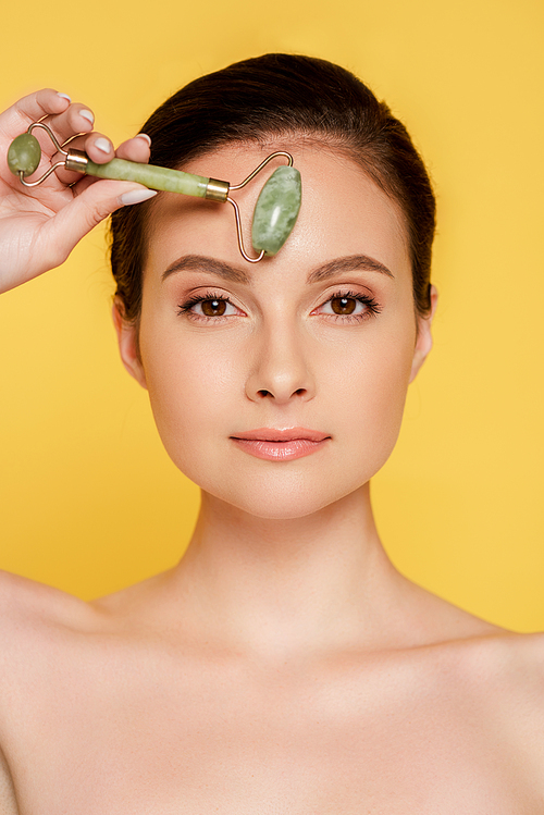 beautiful naked woman using jade roller on face isolated on yellow