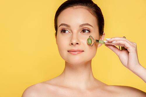 beautiful naked woman using jade roller on face isolated on yellow