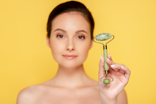 selective focus of beautiful naked woman holding jade roller isolated on yellow