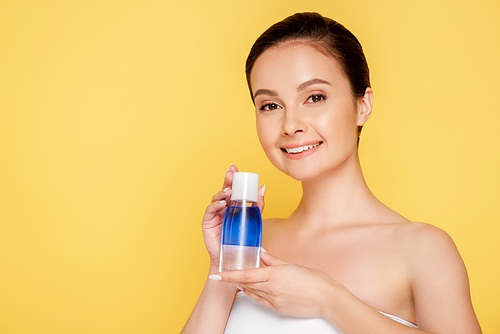 smiling beautiful woman holding micellar water in bottle isolated on yellow
