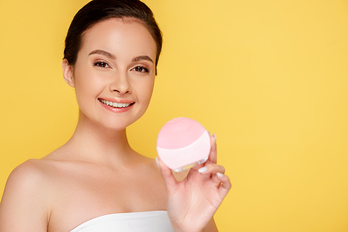 smiling beautiful woman holding facial cleansing brush isolated on yellow