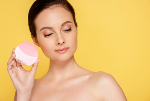 beautiful naked woman holding facial cleansing brush isolated on yellow