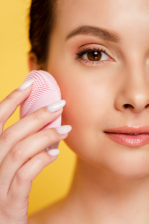 close up view of beautiful woman using facial cleansing brush isolated on yellow