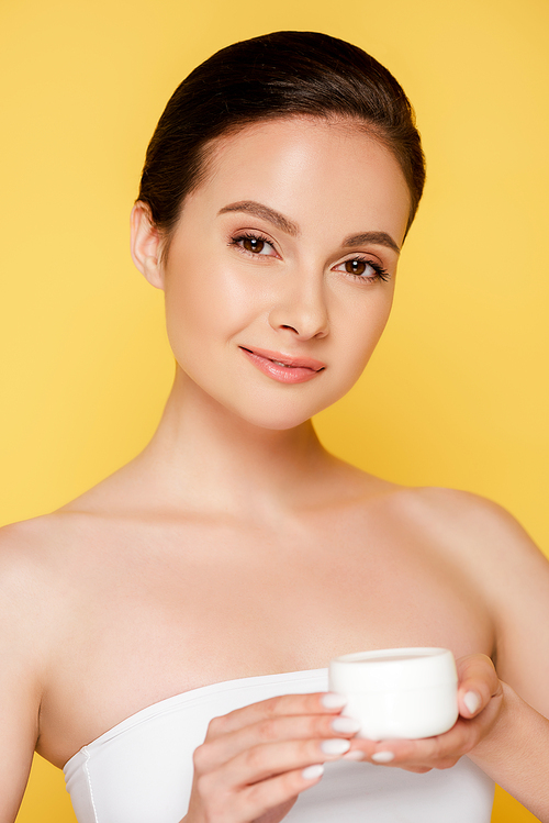 smiling beautiful woman holding container with cosmetic cream isolated on yellow