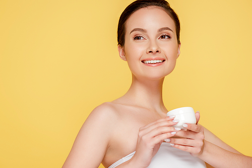 smiling beautiful woman holding container with cosmetic cream isolated on yellow
