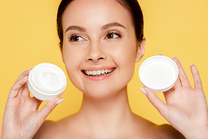 smiling beautiful naked woman holding container with cosmetic cream isolated on yellow