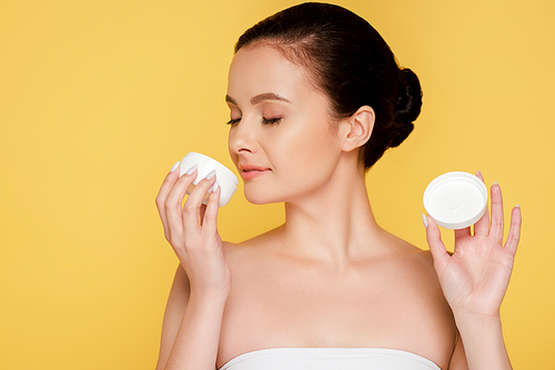 beautiful woman smelling cosmetic cream isolated on yellow