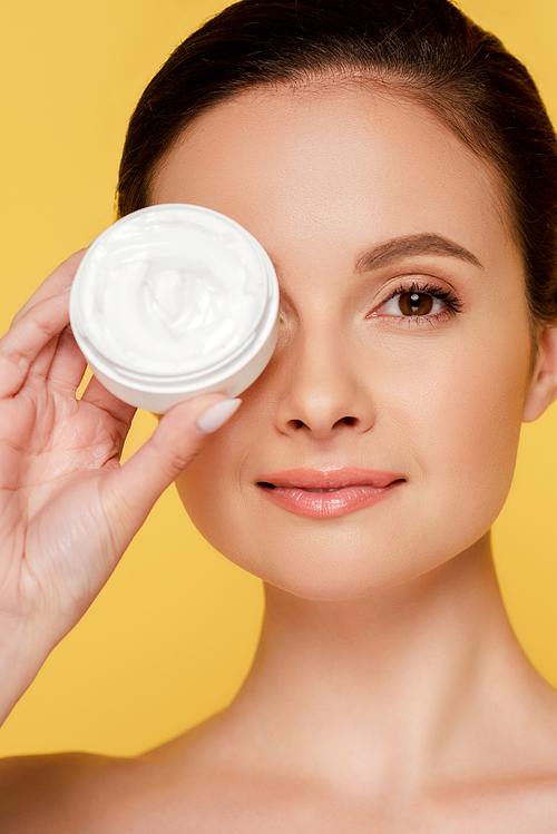 portrait of beautiful naked woman holding container with cosmetic cream isolated on yellow