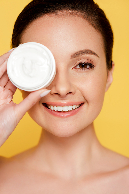 portrait of smiling beautiful naked woman holding container with cosmetic cream isolated on yellow