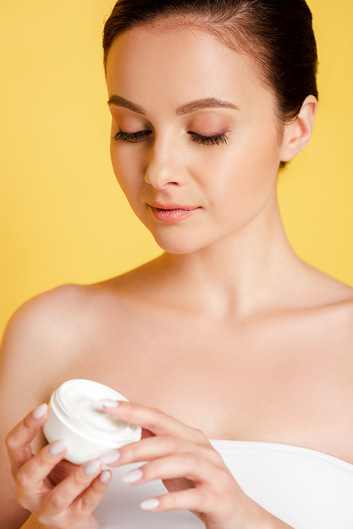 beautiful woman holding container with cosmetic cream isolated on yellow