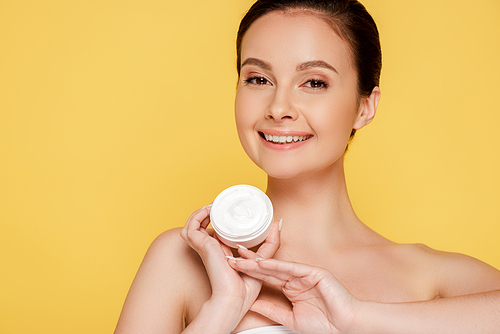smiling beautiful naked woman holding container with cosmetic cream isolated on yellow