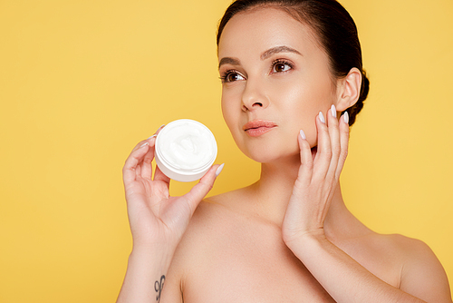 beautiful naked woman holding container with cosmetic cream isolated on yellow