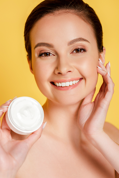 happy beautiful naked woman holding container with cosmetic cream isolated on yellow